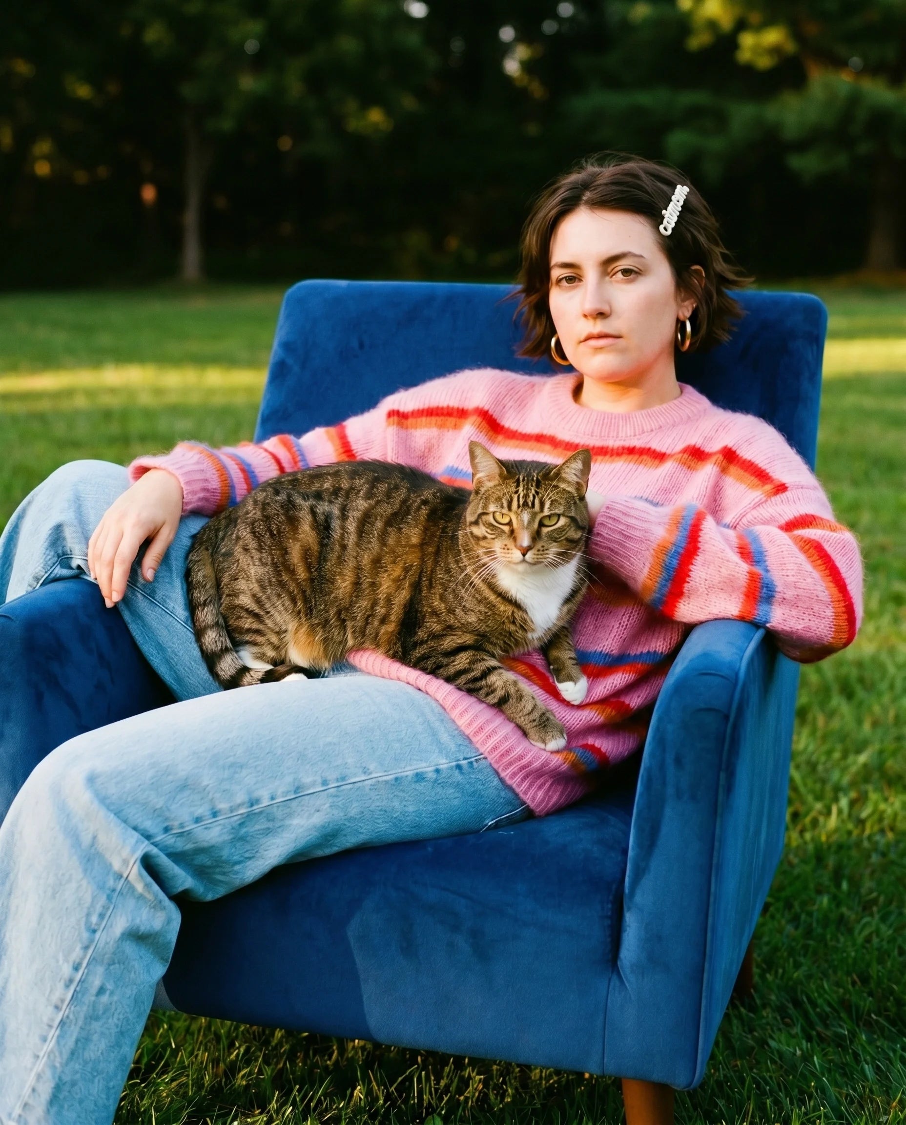 Woman in a pink sweater with a cat on her lap, sitting in a blue chair outdoors.